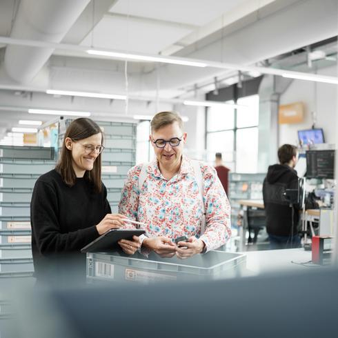 An employee and a female employee of Testo work together at their desks and look into the camera together.