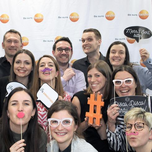 Testo employees laugh happily into a photo box