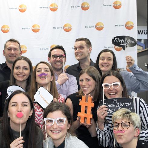 Testo employees laugh happily into a photo box